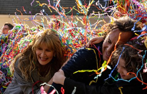 People laughing and hugging while covered in colorful streamers. From L to R: Laura Dern, Will Arnett, and Calvin Knegten in IS THIS THING ON?