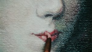Close up of a paint brush with paint adding colour to lips 