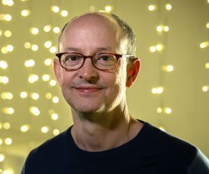 Ed Guiney smiling infront of a fairy light wall