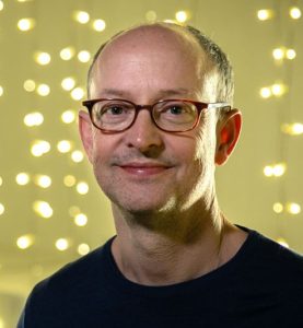Ed Guiney smiling infront of a fairy light wall