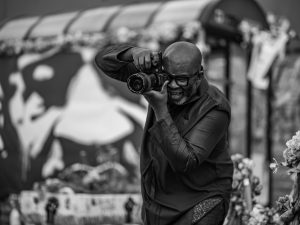 Black and white image of a man (Misan Harriman) holding a camera, shooting an image infant of a mural