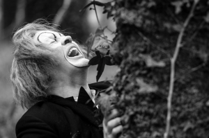 A man in clown Makeup, throwing his head back laughing 