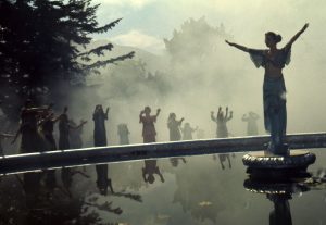 Group of people worshipping person in the centre of a lake with their hand up 